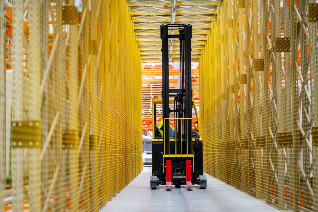 Viljuškar u uskom skladišnom prolazu sa visokim policama, optimizovan za efikasan rad. Industrijska oprema viljuškari i viljuškari oprema za skladište poboljšavaju produktivnost i sigurnost.