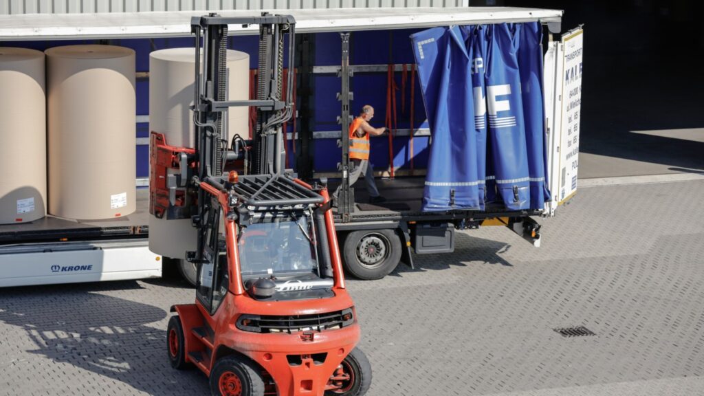 Viljuškar istovara robu ispred kamiona, ljudi rade u blizini; Linde Safety Guard smanjuje rizik u gužvi.