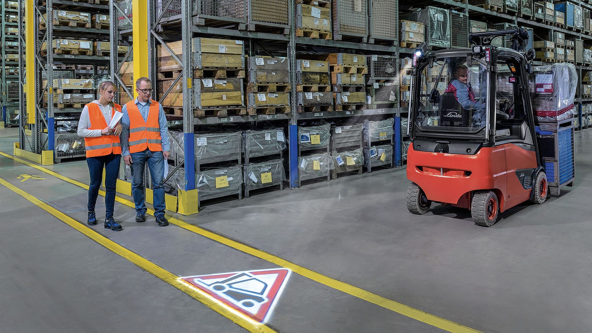 Linde TruckSpot projektuje svetlosni znak na podu magacina radi upozorenja pešaka dok viljuškar prolazi pored radnika u skladištu
