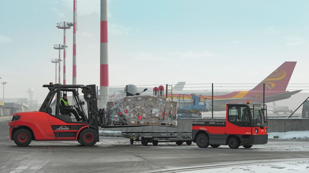 Linde viljuškar i tegljač transportuju teret na aerodromskoj pisti ispred aviona