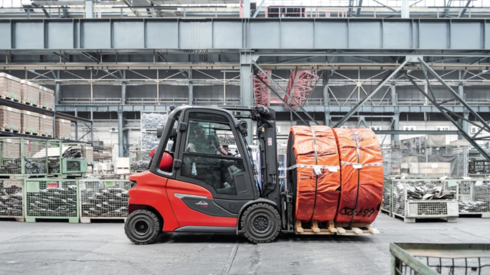Linde viljuškar transportuje narandžasto upakovane koturove u industrijskom magacinu