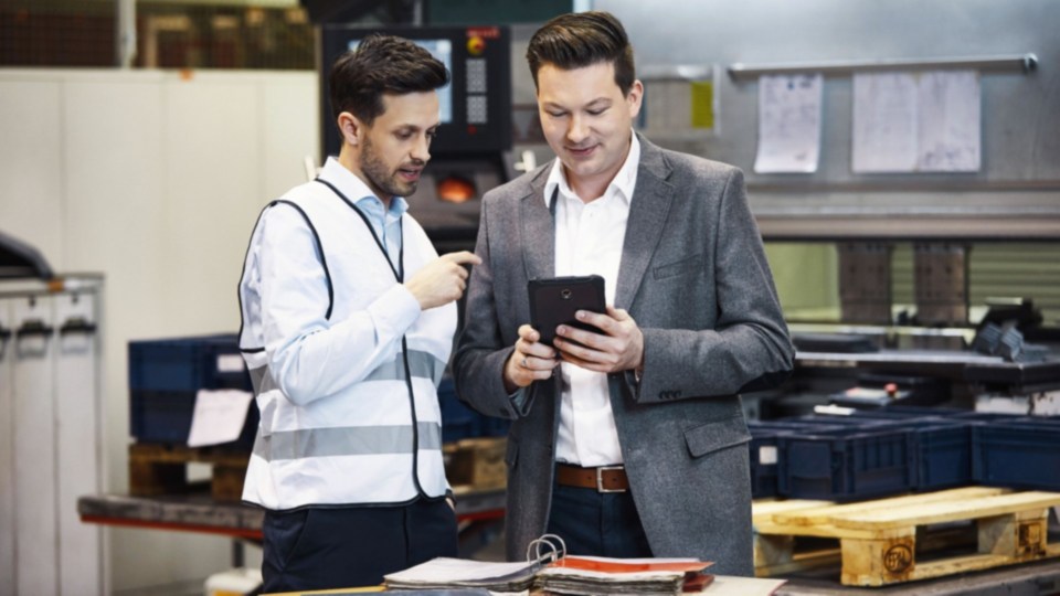 Menadžer skladišta i inženjer posmatraju različite opcije za tehnički i bezbednosni servis na tabletu
